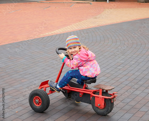 Little girl having fun driving a pedal car in day.