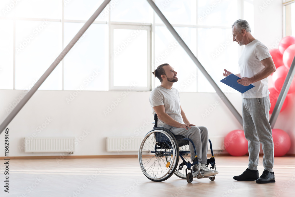 Smiling young disabled patient having conversation with his physical therapist
