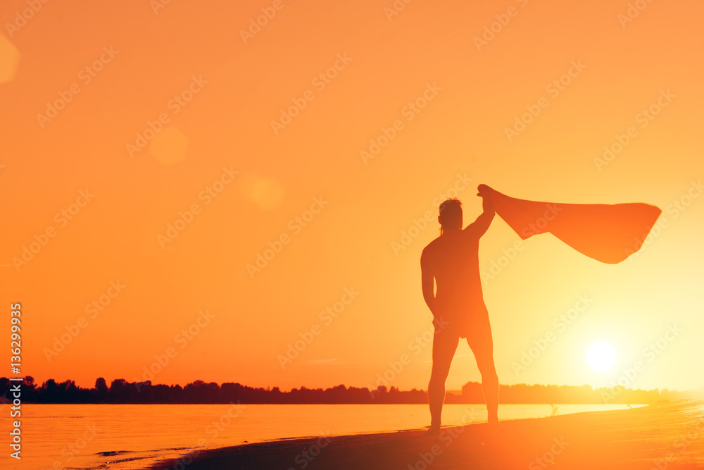 Silhouette of a naked man with a towel on the beach at sunset Silhouette of a naked man with a towel on the beach at sunset
