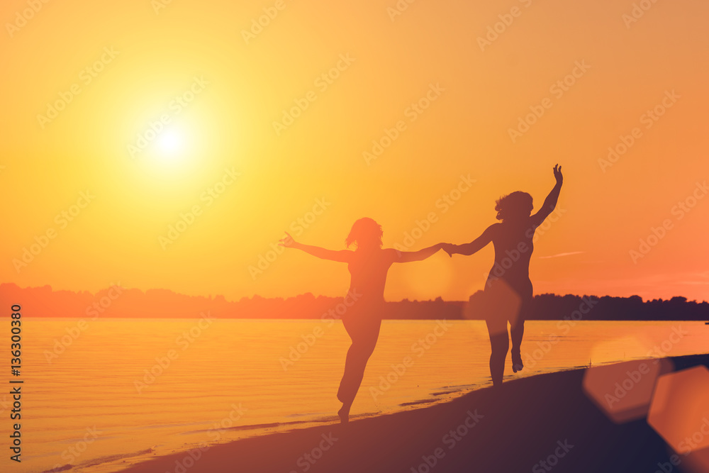Fototapeta premium Silhouette of a woman holding hands running on the beach at sunset