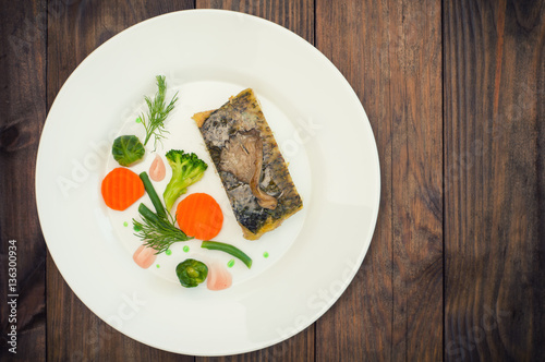 Fototapeta Naklejka Na Ścianę i Meble -  Tasty baked fish on plate on table close-up. Wooden background. Top view. Close-up