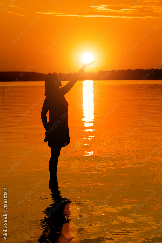 Woman is holding sun  in water at sunset