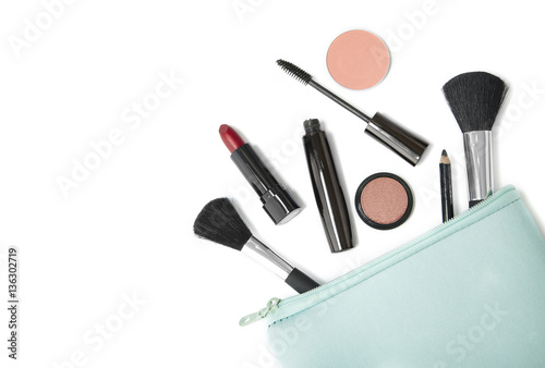 Make up products spilling out of a pastel blue cosmetics bag, isolated on a white background and blank space at side