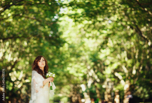 The bride with bouquet stands in the park