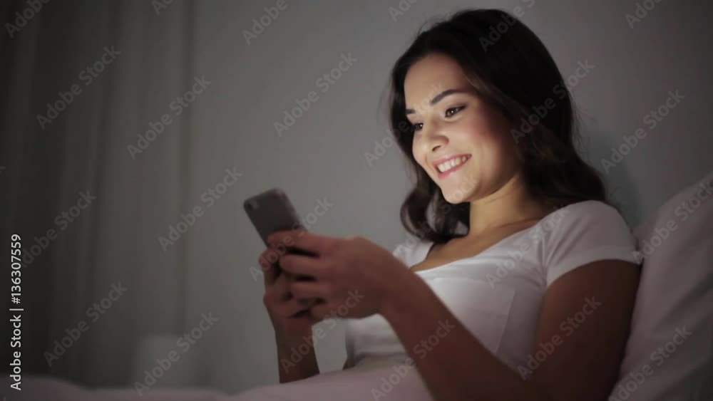 happy young woman with smartphone in bed at night happy young woman with smartphone in bed at night