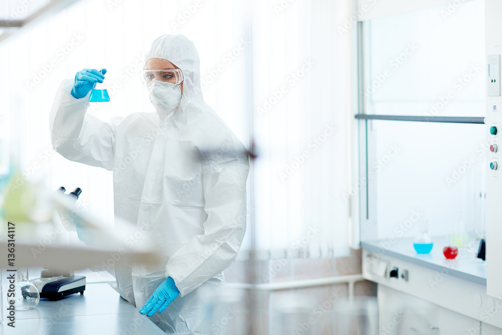 Pharmacologist in protective overalls looking at dangerous toxic fluid Pharmacologist in protective overalls looking at dangerous toxic fluid
