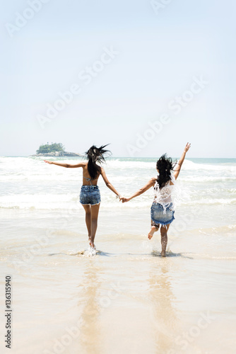 Brazil, Sao Paulo, Ubatuba, two young women running on the beach holding hands photo