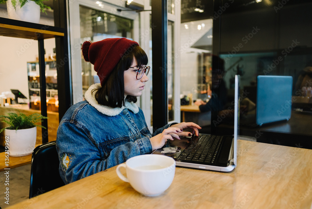 Fototapeta premium portrait of a girl hipster who uses a laptop in a cafe