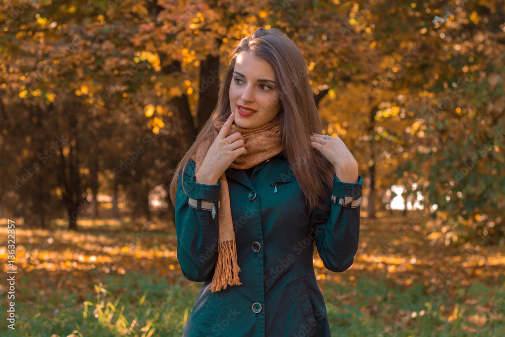 cute young girl in a dark jacket and scarf stands in the Park looks away cute young girl in a dark jacket and scarf stands in the Park looks away