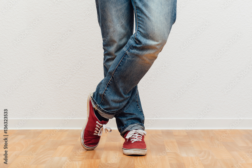 Mann steht mit gekreuzten Beinen vor einer Wand, untere Körperhälfte Mann steht mit gekreuzten Beinen vor einer Wand, untere Körperhälfte