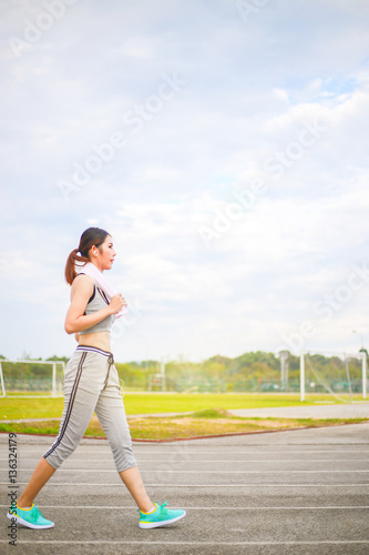 Young woman wearing sports clothes and towels, sport women walking listening to music with headphones in the stadium, is smiling and happy