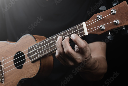 Man playing ukulele finger stlye with chord on black background