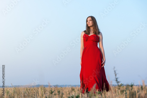 Gorgeous young woman in red dress walking in golden field