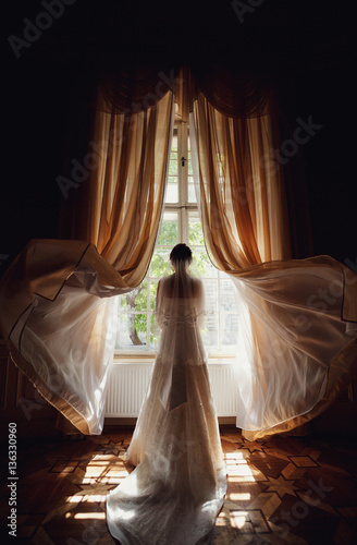 bride in a white dress with a long train standing at the window