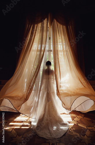 bride in a white dress with a long train standing at the window
