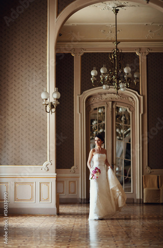 bride holding train of her dress in beautiful hall