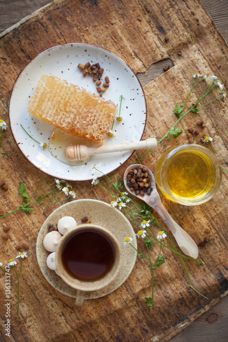 Serving table  drawn honey comb with honey dipper on a ceramic plate with cup of black tea.