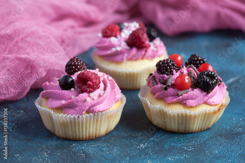 Homemade vanilla cupcakes with multicolor cream cap and berries on a dark blue background.