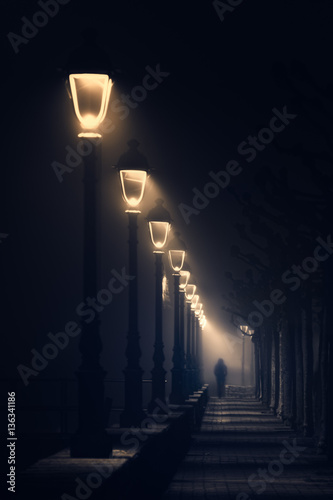 person walking on dark street illuminated with streetlamps photo