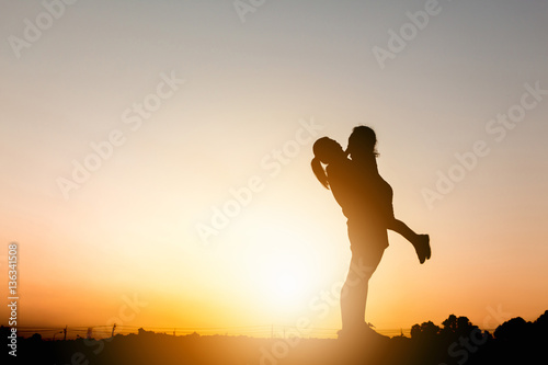 Silhouettes of mother and daughter playing at sunset evening sky background.