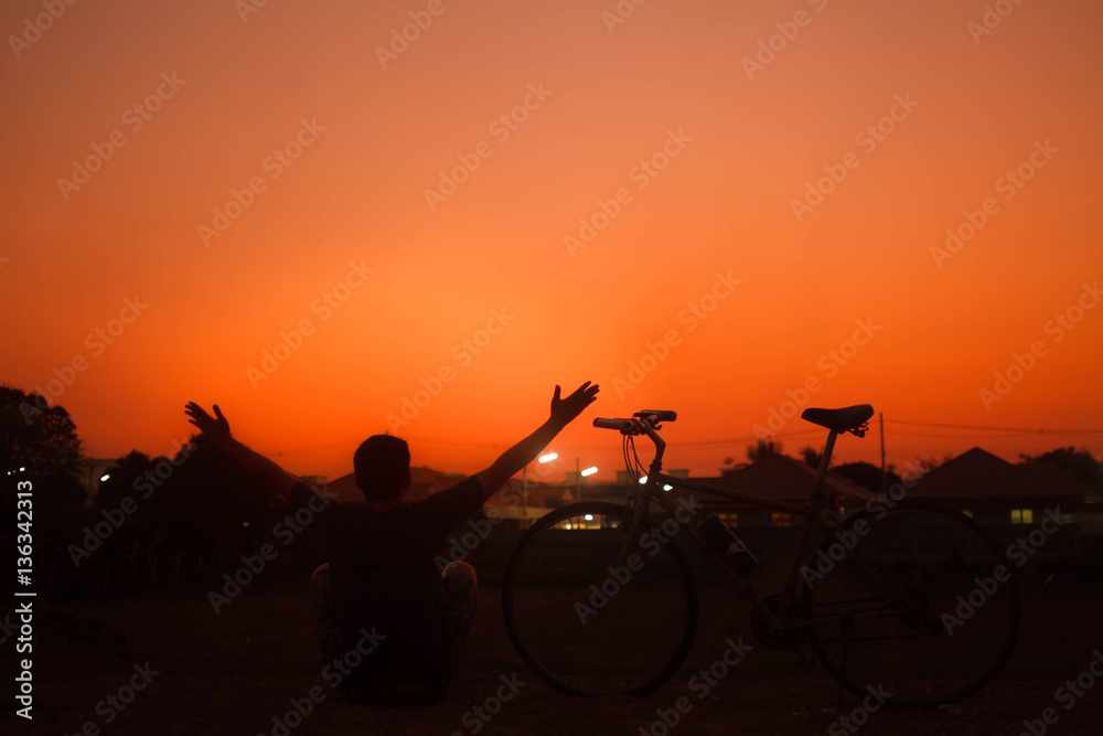 Silhouette freedom man sitting near bicycle on sunset.