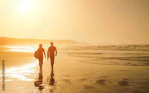 Couple of surfers leaving the water after surfing on a beautiful sunset at the beach. Body board and surf lifestyle concept.