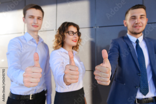 Three beautiful young people showing thumbs up, laughing, smilin photo