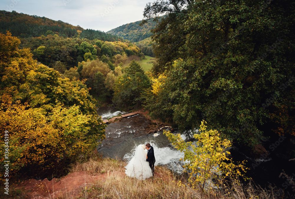 Fototapeta premium Beautiful stylish newlyweds posing near the river outside