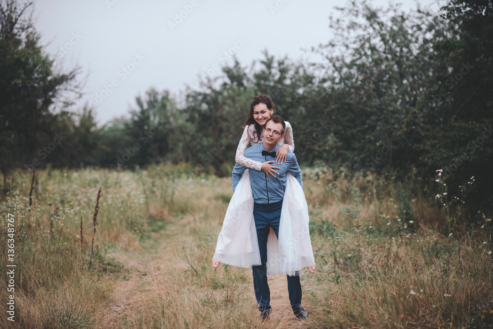 Just married loving hipster couple in wedding dress and suit on a green field in the woods. happy bride and groom walking running and dancing on a summer meadow. Romantic married to a young family Just married loving hipster couple in wedding dress and suit on a green field in the woods. happy bride and groom walking running and dancing on a summer meadow. Romantic married to a young family