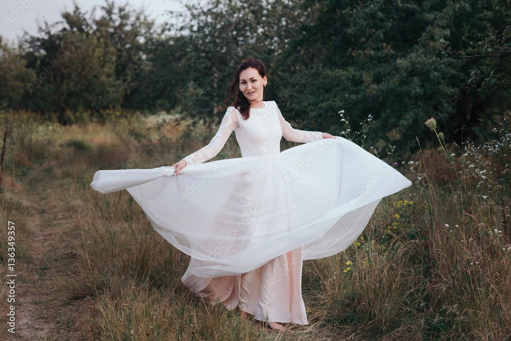 Yong bride spinning in a white dress on the bank on nature.Dress develops in the wind. Happy bride in a wedding dress is spinning. Yong bride spinning in a white dress on the bank on nature.Dress develops in the wind. Happy bride in a wedding dress is spinning.