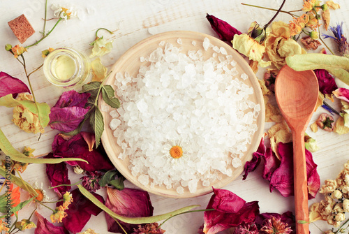 Sea salt mineral grains on round wooden plate dried petals medicinal plants. Herbal aroma bath salt blend. toned. 