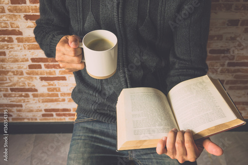 Closeup of a young man reading a book while drinking coffee from