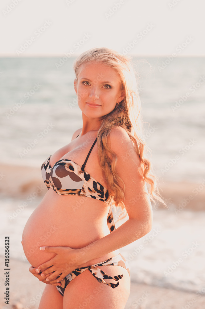 Smiling pregnant woman 25-30 year old wearing stylish swimsuit over sea  background. Looking at camera. Maternity. Stock Photo | Adobe Stock