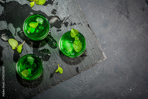 Sweet refreshing mint liqueur, with ice and mint leaves on the slate tray to feed on gray concrete stone table, top view, copy space