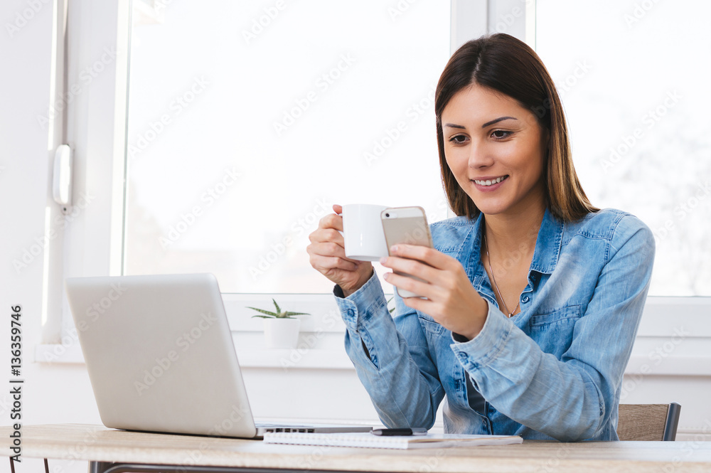 Smiling young woman holding a mug and texting with smartphone Smiling young woman holding a mug and texting with smartphone