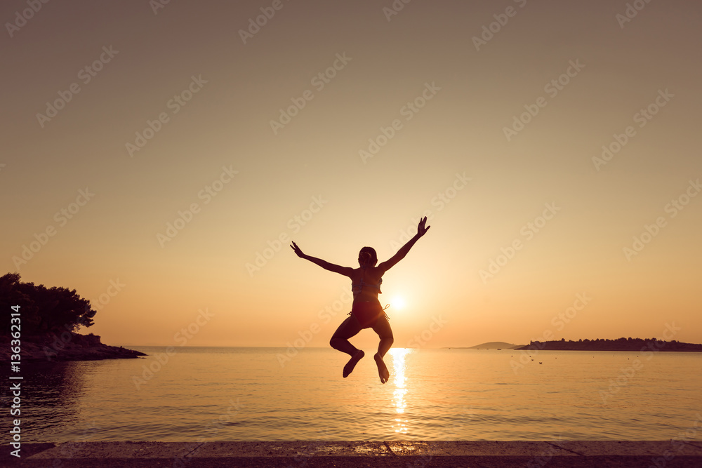 Child little girl is jumping into the sea from a pier at sunset