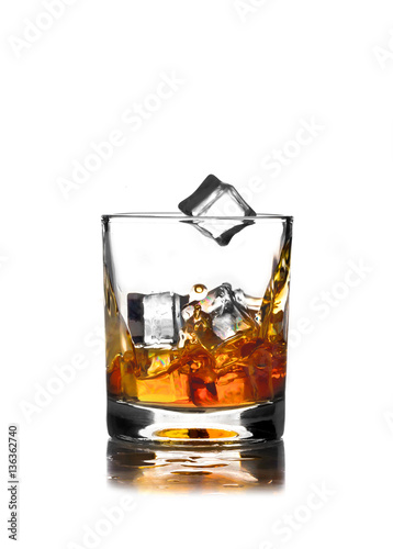 glass of whiskey on a white background with an ice cube that falls into alcohol