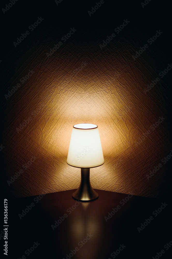 Table top lamp with burlap shade lit on a wooden table and a bottle of male perfume. Table top lamp with burlap shade lit on a wooden table and a bottle of male perfume.