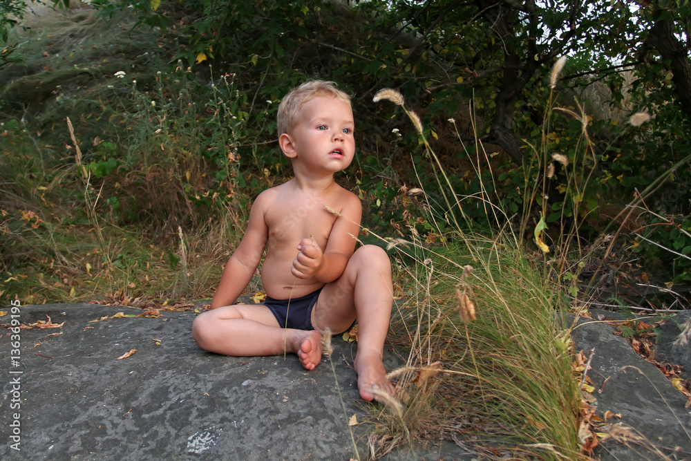 Small white Toddler sitting on a big gray stone and curiously an Small white Toddler sitting on a big gray stone and curiously an