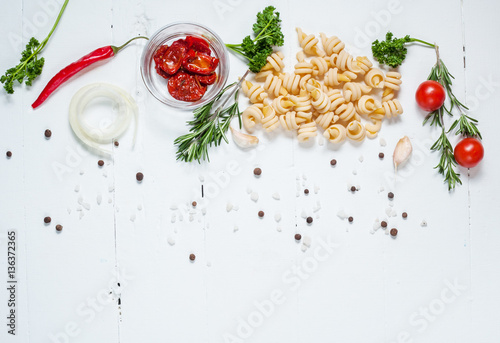 Background with pasta, tomatoes cherry and herb on white wooden table. Place for text.