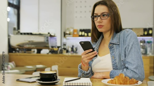 Young beautiful woman using mobile phone, texting massege, sending sms while sitting in cafe