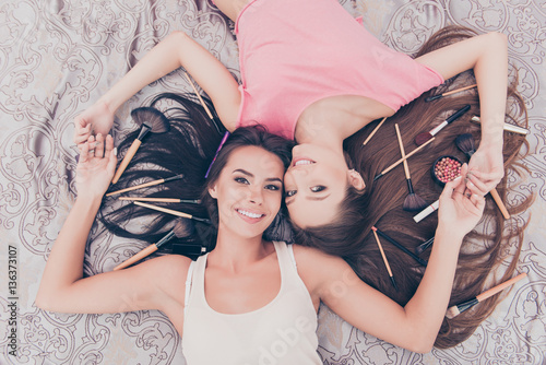 Top view of two pretty girls lying with cosmetics and makeup bru photo