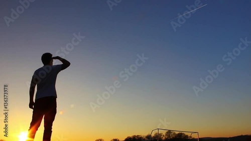 Silhouette of man looking up at plane trails, sunset