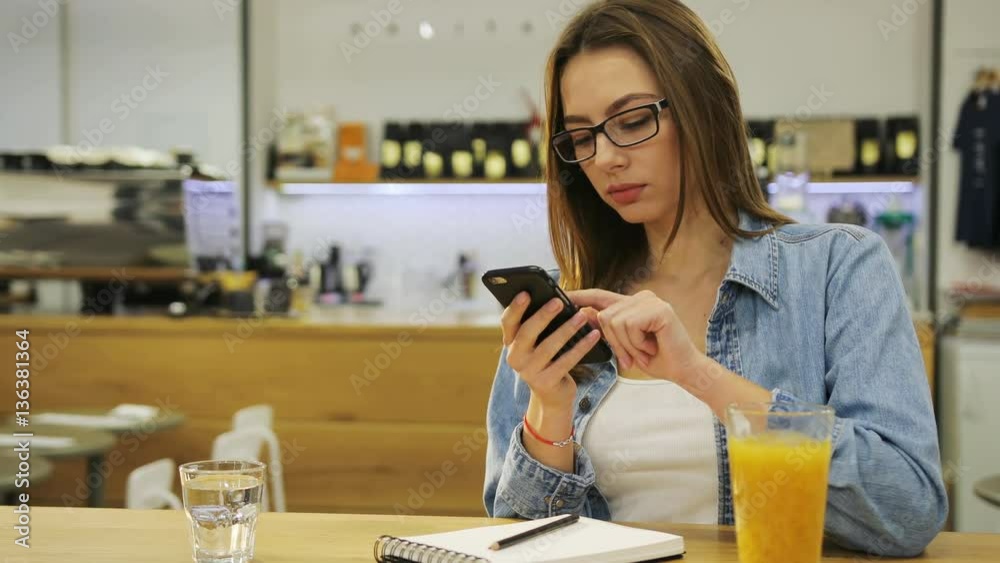 Young beautiful woman typing on smartphone, surfing the internet and drinking juice in cafe Young beautiful woman typing on smartphone, surfing the internet and drinking juice in cafe