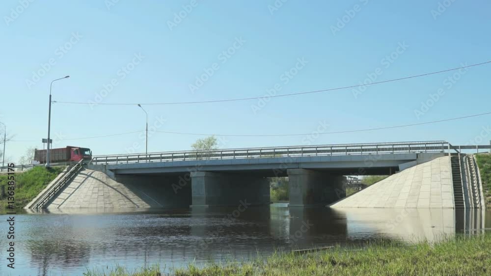 Different cars going on bridge over small river on clear sunny day in city Different cars going on bridge over small river on clear sunny day in city