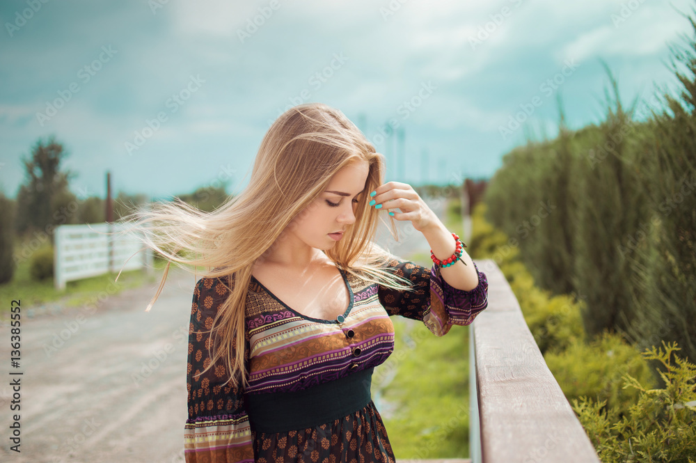 Stylish Portrait of a beautiful girl in a dress that straightens hair fluttering in the wind. On open air. Vintage clothing. Retro. Farm.