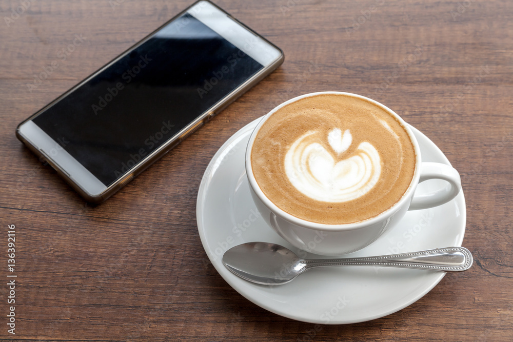 Coffee cup of latte art with smartphone on wooden background