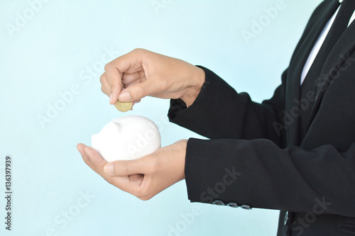 Businesswomen holding coin and white piggy bank on blue background selective and soft focus 