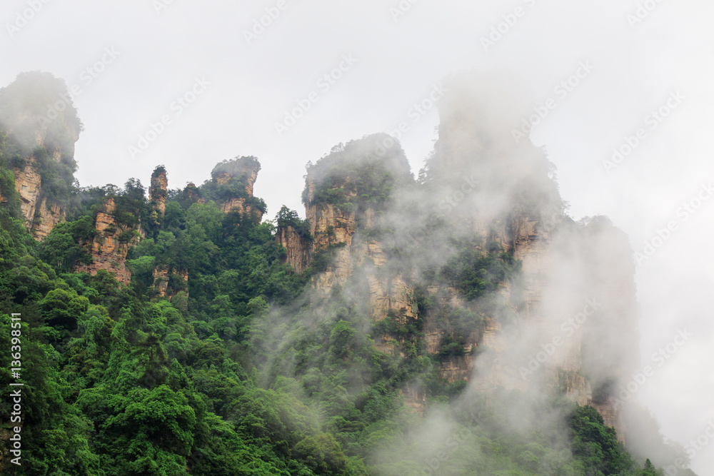 Photo of Huge Rock Mountains Surrounded by Green Trees and White Mist Clouds. Epic Mountain Landscape