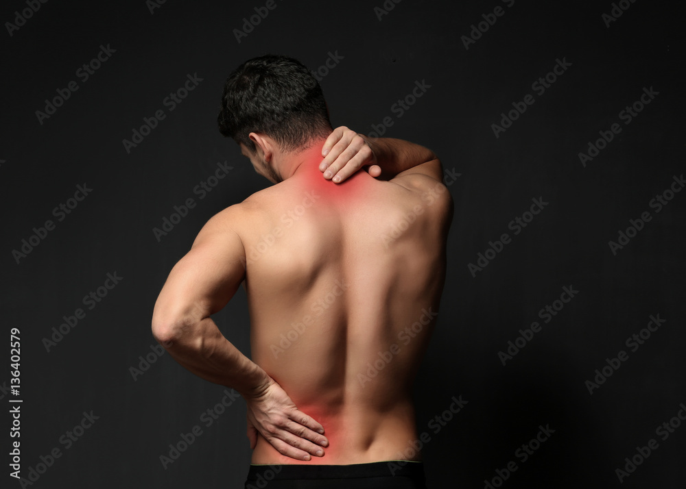 Young man suffering from back pain on black background. Health care concept Young man suffering from back pain on black background. Health care concept